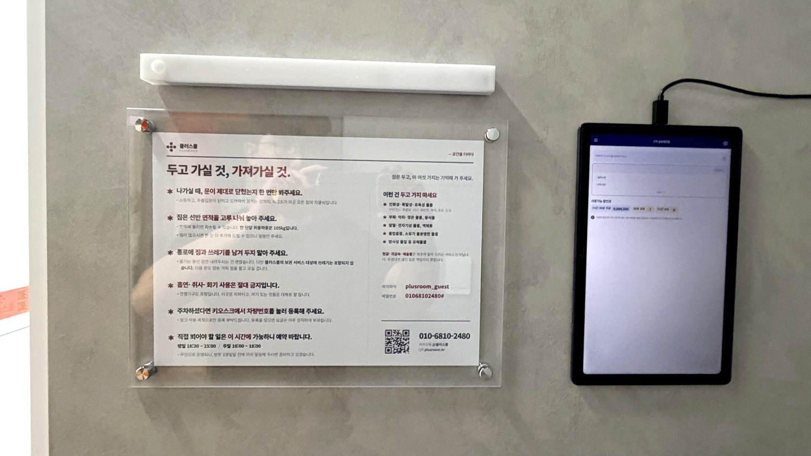 주출입문 안쪽 벽에 부착된 창고 이용안내판 — 아크릴 액자와 상단 조명